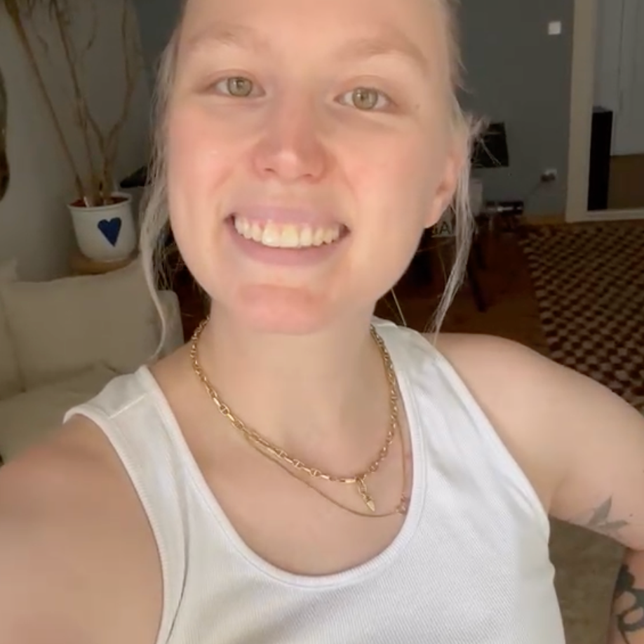 Blonde Frau im weißen Top lächelt in einer Videobotschaft