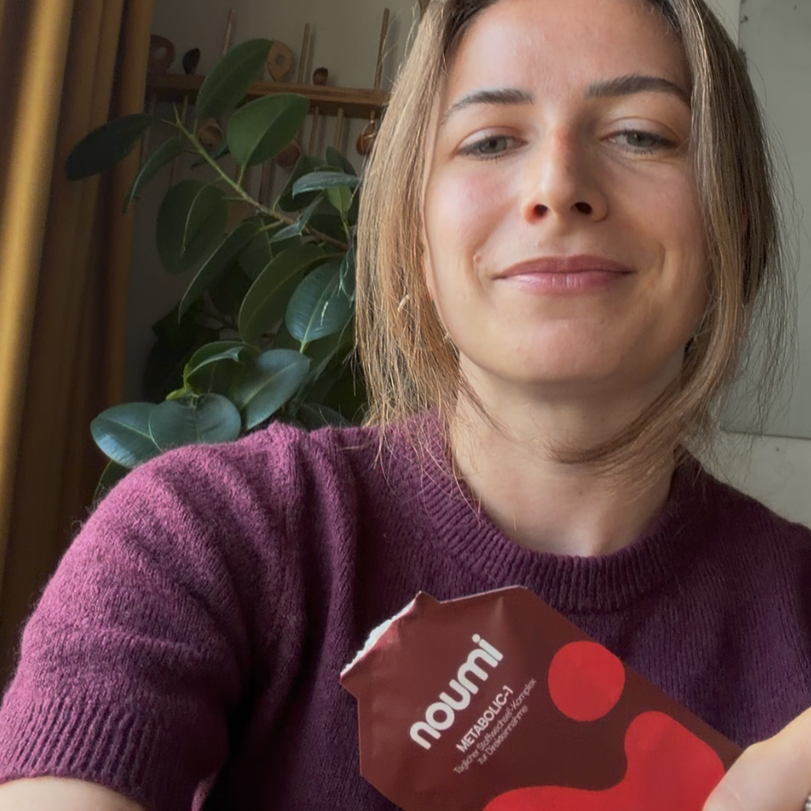 Frau in lila Pullover hält ein noumi Metabolic-1 Sachet in die Kamera