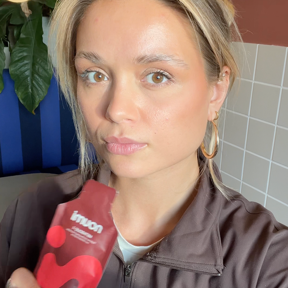 Frau mit blonden Haaren und goldenen Creolen hält ein rotes noumi Metabolic-1 Sachet