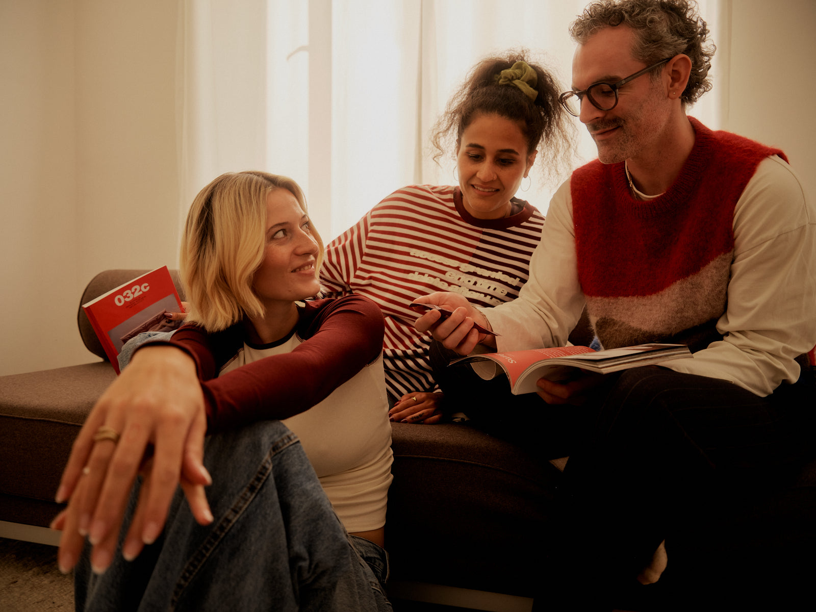 Drei Personen in einer Sitzecke betrachten gemeinsam ein aufgeschlagenes Magazin