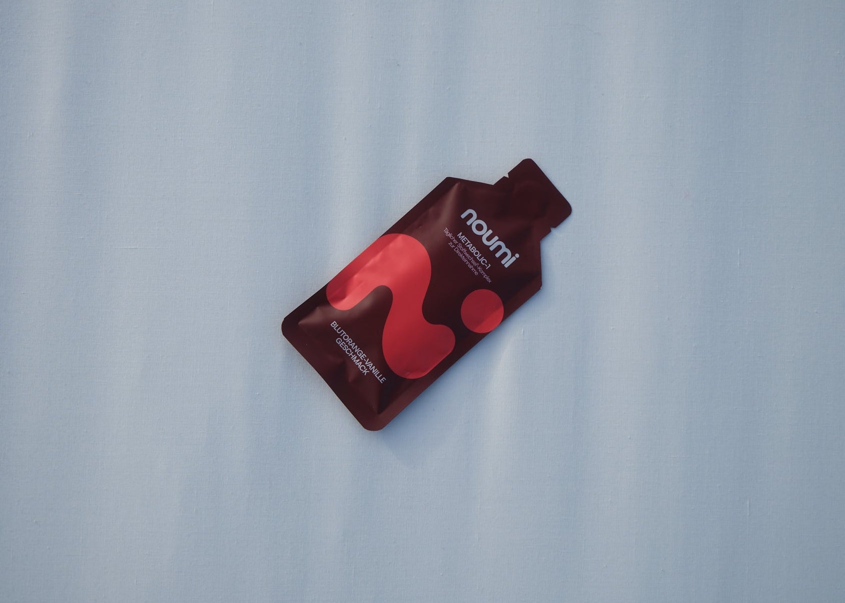 noumi Metabolic-1 Gel-Sachet liegt auf einer hellblauen Fläche, Ansicht von oben