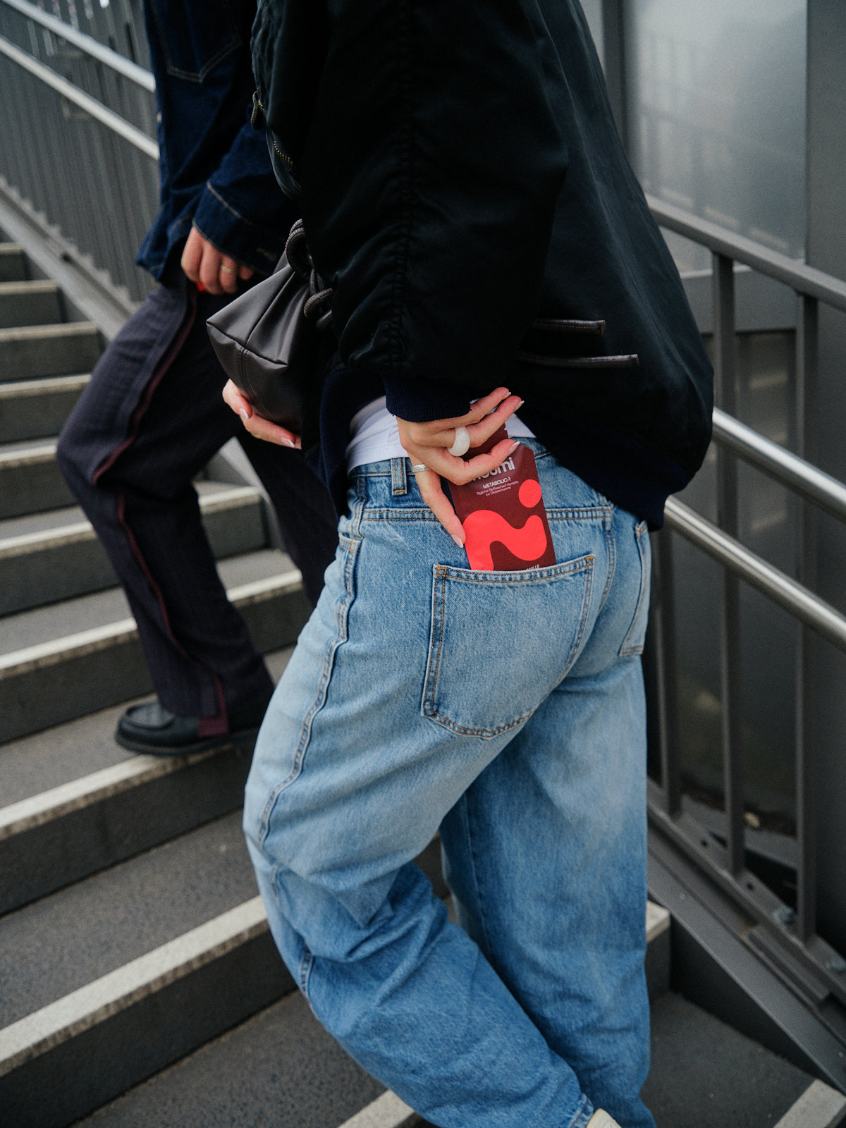 Person steigt eine Treppe hinauf, noumi Metabolic-1 Sachet in der Gesäßtasche
