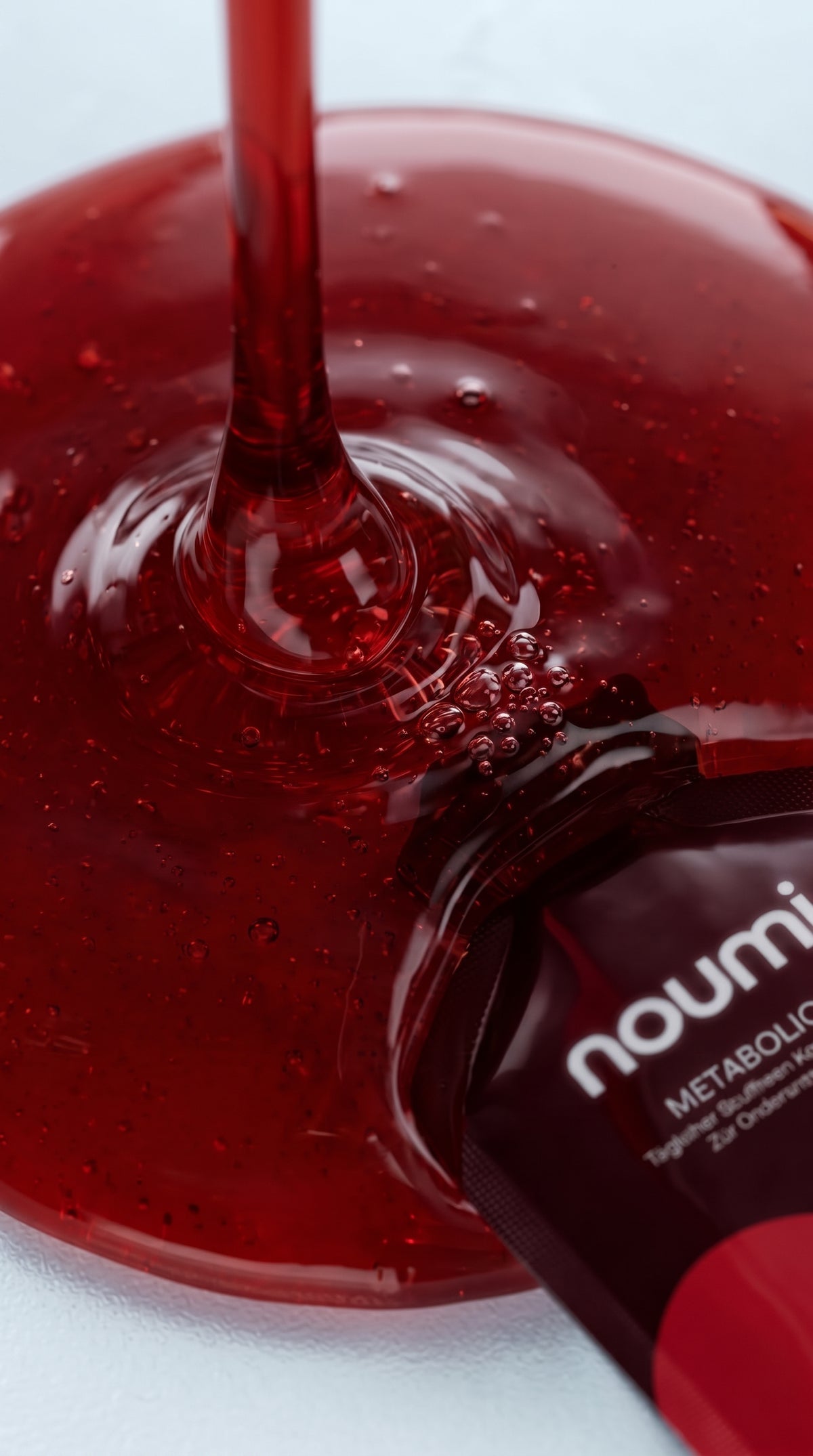 Rotes noumi Metabolic-1 Gel fließt in eine Glasschale neben einem Gel-Sachet